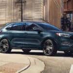 A blue 2024 Ford Edge ST rounding the corner of a city street.