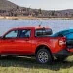 A red 2024 Ford Maverick is parked near a pond with a kayak in the bed.
