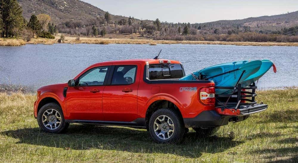 A red 2024 Ford Maverick is parked near a pond with a kayak in the bed.