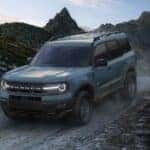 A blue 2024 Ford Bronco Sport Big Bend driving down a hill on a dirt road.