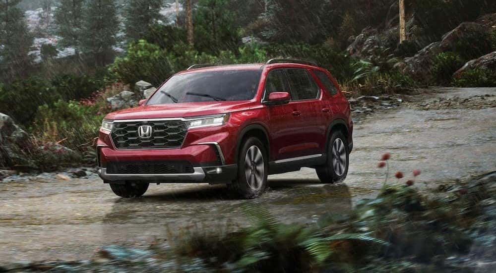 A red 2025 Honda Pilot is shown driving on a rainy day.