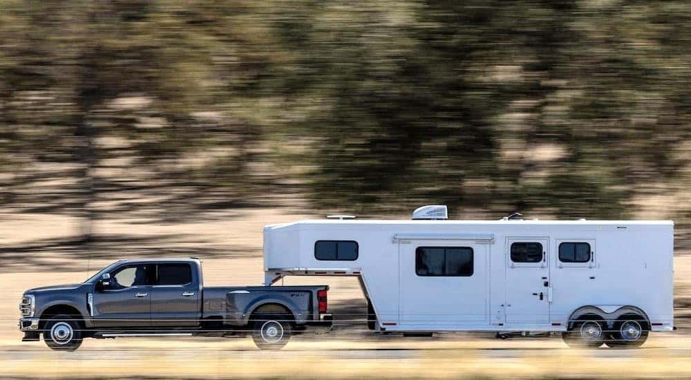A grey 2023 Ford F-350 is shown from the side while towing a horse trailer after leaving a dealer with used trucks for sale.