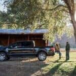 A black 2025 Ford F-150 XLT is shown parked on a farm.