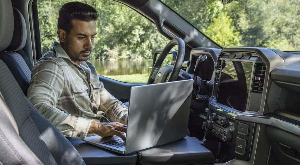 A person is shown using a laptop in a Ford F-150 for sale near Pueblo.
