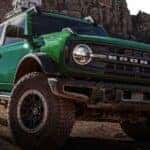 A green 2025 Ford Bronco driving off-road on a dirt road.