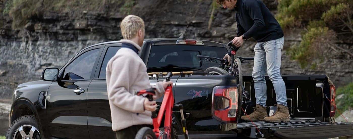 Rear view of people unloading bicycles from the bed of a black 2024 Ford Ranger XLT.