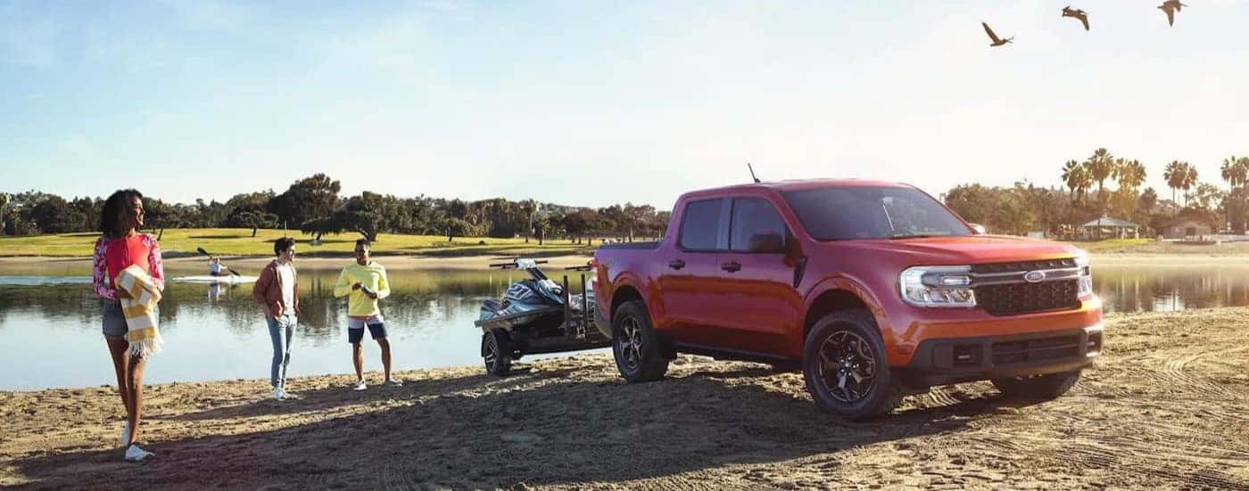 A red 2023 Ford Maverick FX4 towing a trailer near a pond.