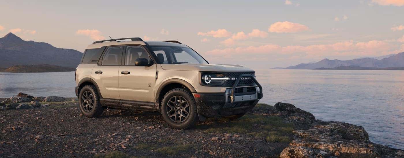 A tan 2025 Ford Bronco Sport Big Bend parked near a lake and mountains.