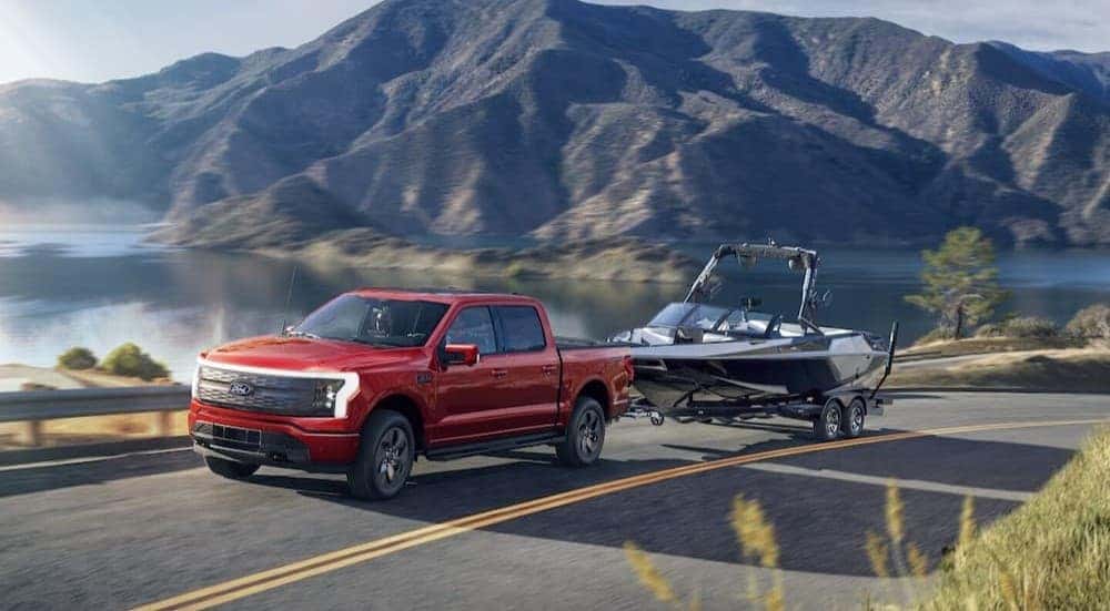 A red 2025 Ford F-150 Lightning towing a boat on a highway.