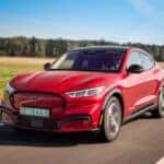 All-electric bright red Ford Mustang Mach-E drives on a highway during a sunny day.