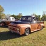 Old black and orange 1956 Ford F 100 V8 pickup truck on the lawn at a classic car show in a park
