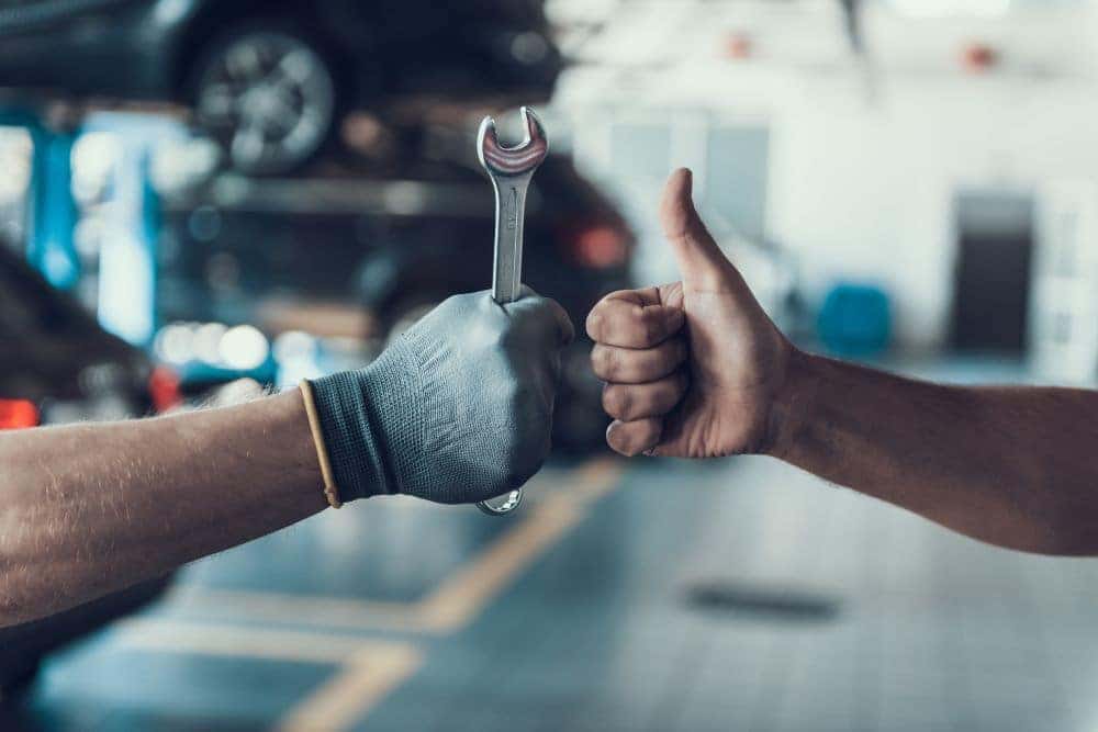 One hand holding a wrench the other holding its thumb up.