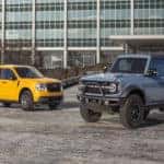 Yellow Ford Maverick pickup Blue Ford Bronco outside building
