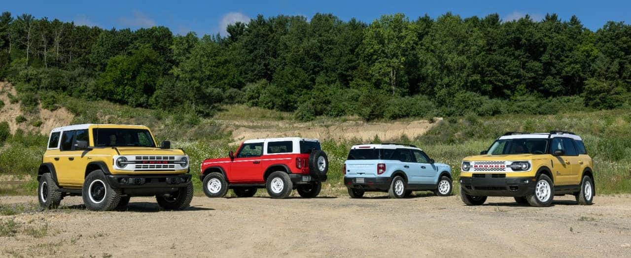Four Ford Bronco SUVs Outside green trees