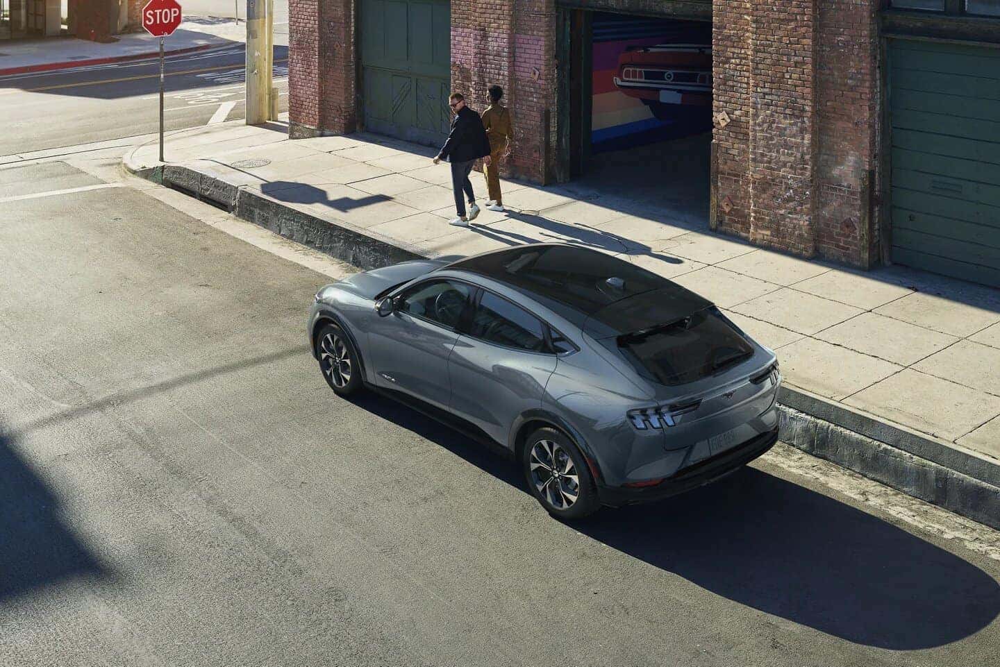 Gray Ford Mustang Mach-E EV SUV Outside Building Two People