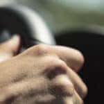 Close-up of a hand wrapped around a black steering wheel