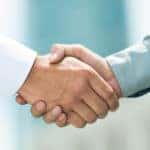 Close-up of man in a white shirt shaking hands with a man in a blue shirt