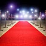 Red carpet with red velvet ropes on either side and lights at the end