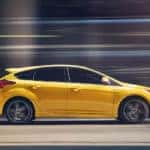 A yellow 2018 Ford Focus ST is shown from the side driving down a city street.