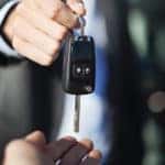 Man in a black suit and white button-up placing a black car key in an open hand
