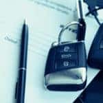 Two black car keys next to a black pen on top of a contract