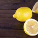 One whole and one cut in-half lemon sitting on a dark brown table