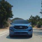 A blue 2019 Ford Edge from the front races down an empty road against a clear blue sky