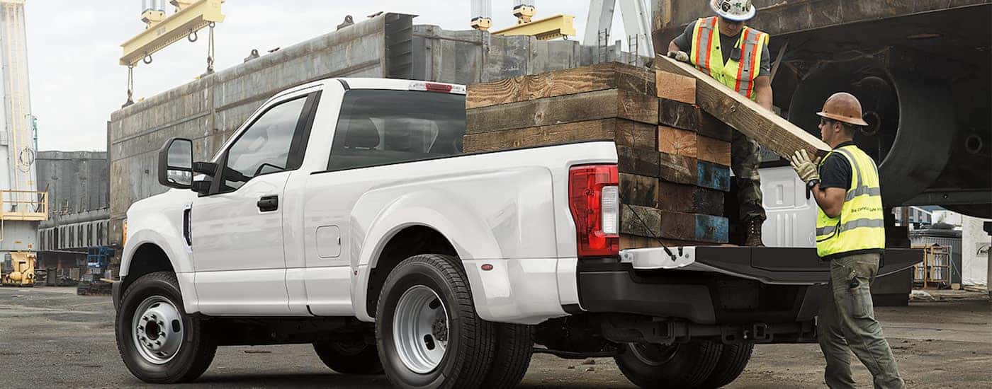 Two men loading lumber into a white 2019 Ford F-250