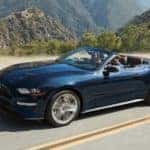 A blue 2019 Ford Mustang convertible cruises a mountain road with the top down
