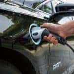 A hand plugging in the charger on a black 2019 Ford Fusion Energi in a driveway