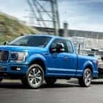 A blue 2019 Ford F-150 is towing a boat past a dam