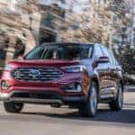 A red 2019 Ford Edge, one of the popular Ford SUVs in Cincinnati, OH, is driving in front of city buildings.