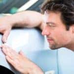 A man is checking the body panel of a car while shopping for used cars in Cincinnati, OH.