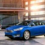 A blue 2018 Ford Focus is parked in front of an office building with a women smiling at it.