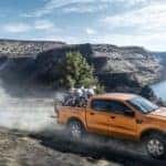 A gold 2019 Ford Ranger, a popular new Ford for sale, is driving on a dirt road with dirt bikes in the bed.