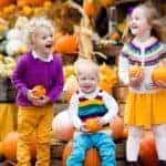 Three kids are at a pumpkin stand.