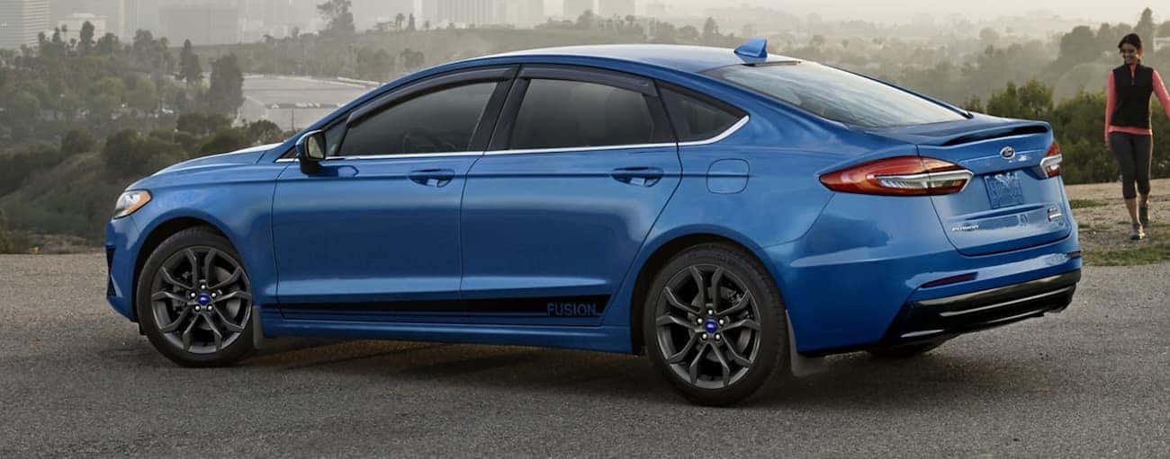 A blue 2020 Ford Fusion is parked with a city in the distance.