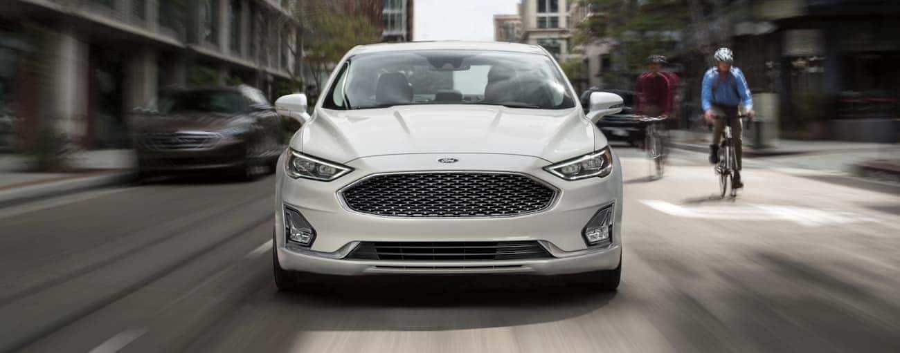 Cyclists are riding up next to a white 2020 Ford Fusion on a city street.