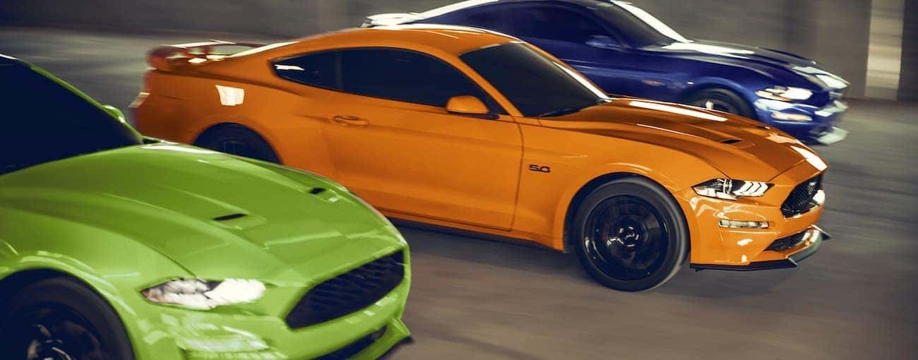 Three 2020 Ford Mustangs in green, orange, and blue are racing.