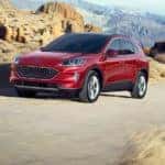 A red 2020 Ford Escape is driving on a dirt road with mountains in the background.