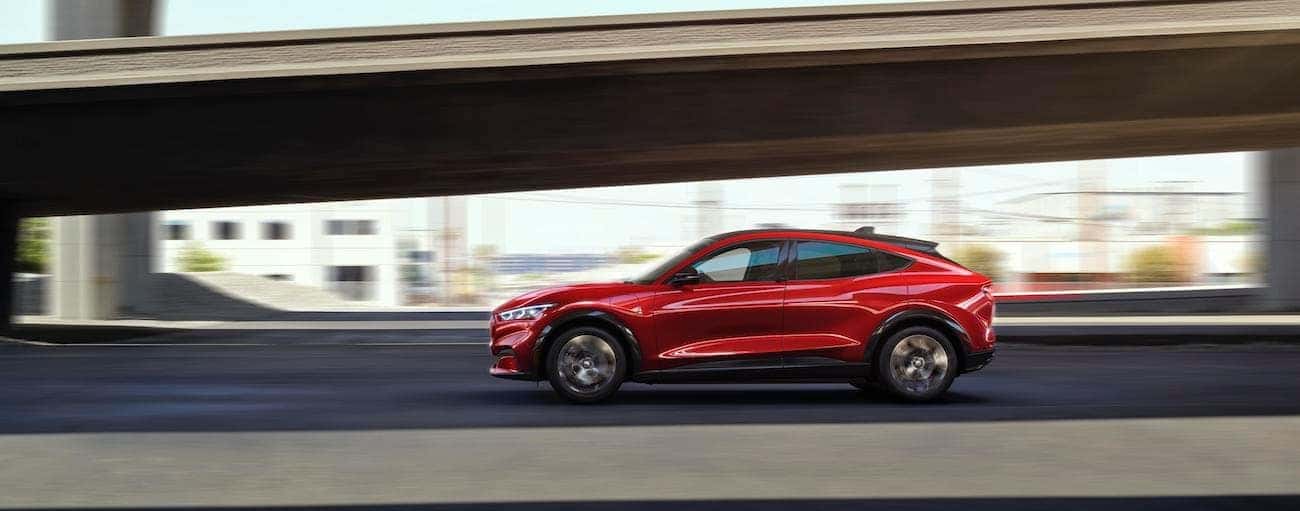 A red 2021 Ford Mustang Mach-E is driving past an over pass in Cincinnati, OH.