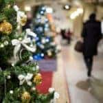 A Christmas tree is lit up with a blurry background of a mall.