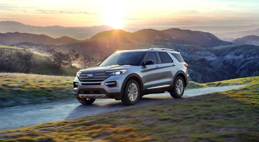 A silver 2020 Ford Explorer is driving with a mountain sunset behind it.