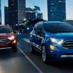 Two Ford SUVs, a red and a blue Ecosport, are driving through Cincinnati, OH, at night.