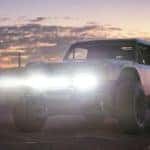 A 2020 Ford Bronco R race prototype has its headlights on as the sun sets behind it.