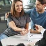 A couple is being handed the keys to a car while at a dealership.