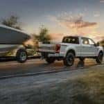 A white 2020 Ford F-250 is towing a boat at sunset.