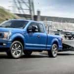 A blue 2020 Ford F-150 STX is towing a boat past a damn.