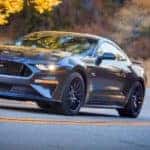 A popular used Ford for sale, a gray 2018 Ford Mustang is driving on a rural highway.