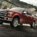 A red 2017 Ford F-150 is towing a boat out of a river.